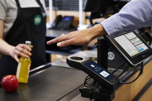 A photo of a customer's hand hovering an Amazon One payment scanner at a Whole Foods check out stand.