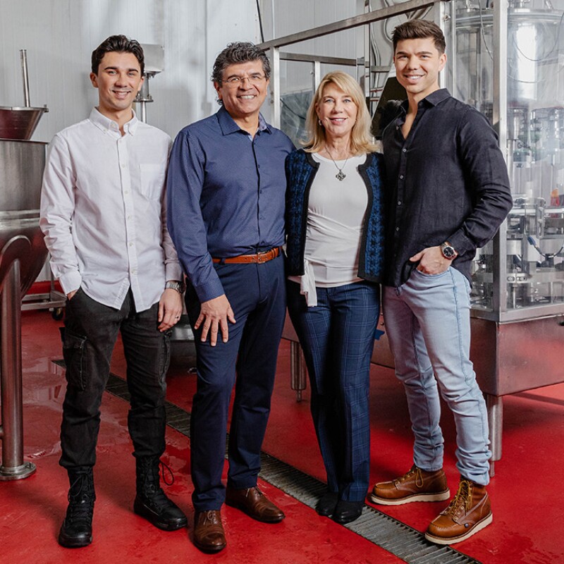 A photo of the family owners of Lucy's Inc. standing in in a factory. There are bottles of apple cider vinegar on a conveyor belt behind them.