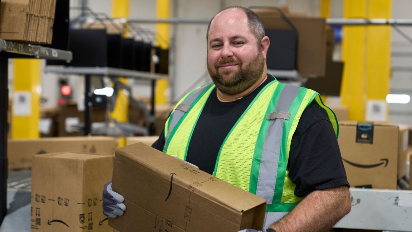 A photo of an Amazon fulfillment center employee holding an Amazon delivery box inside a fulfillment center.