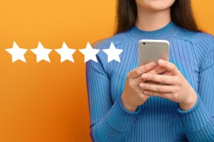 A woman holds up a smartphone to look at it. There are five stars to the left of the woman.