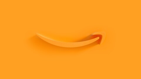 Amazon's orange smile logo appears as an extruded plastic form on an orange background, with a shadow cast by a light source from the right