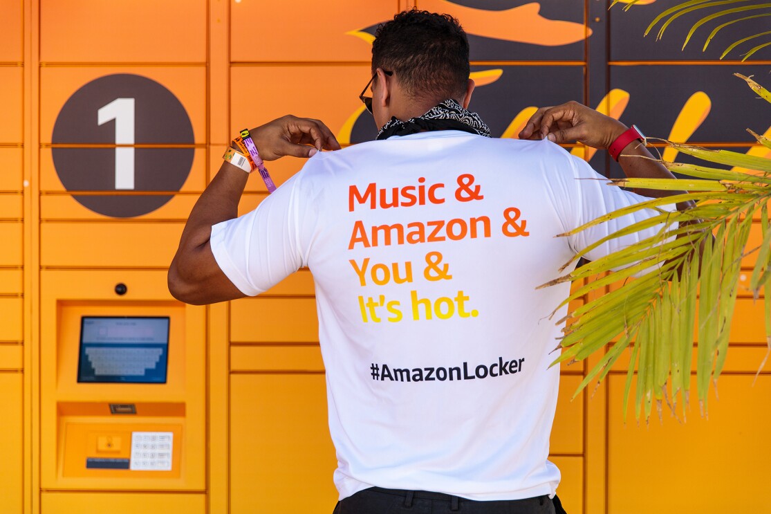 A man wearing a white t-shirt with a message of "Music & Amazon & You & It's hot" printed on the back. He pulls up on the shoulders of the tee as though he's fanning himself. 