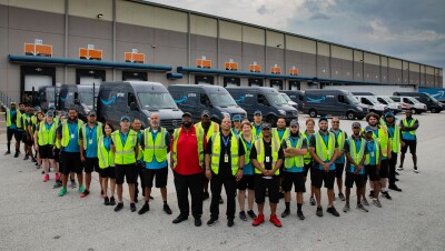 A group of employees stand in front of a fleet of Amazon Prime-branded cargo vans.