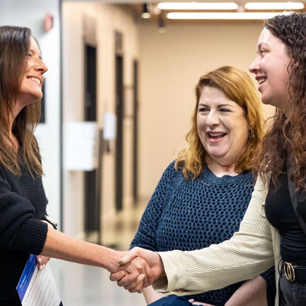 An image of Amazon's Senior Vice President of People Experience, Beth Galetti, shaking hands with employees in a hallway and smiling.