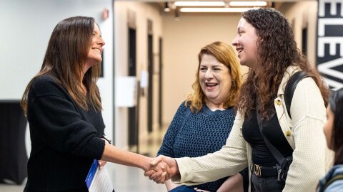 An image of Amazon's Senior Vice President of People Experience, Beth Galetti, shaking hands with employees in a hallway and smiling.