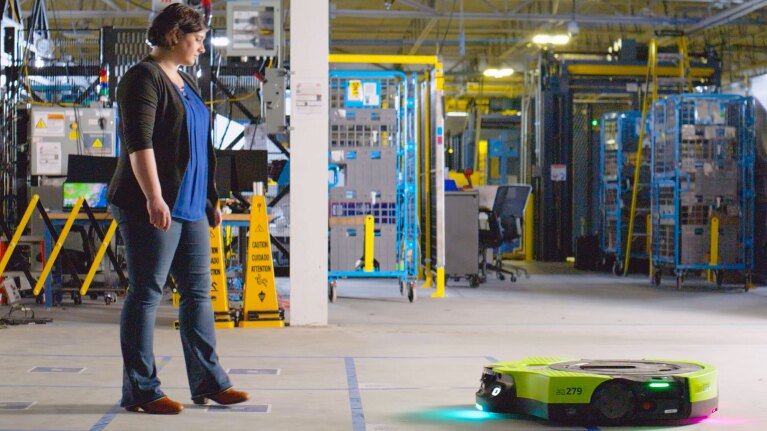 An Amazon employee stands in a fulfillment center and watches Proteus.