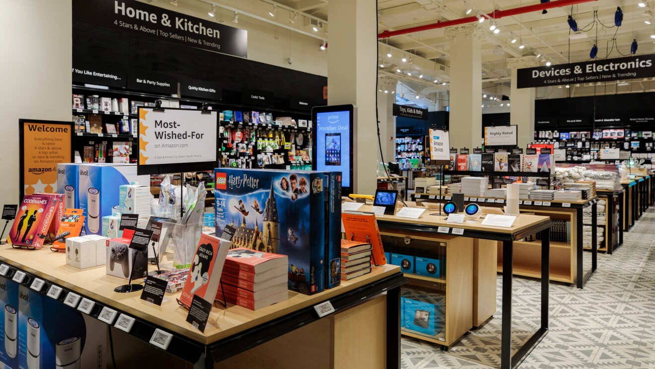 The view inside Amazon 4-star store. Tables are stacked with books, toys, devices, kitchen implements, and cookbooks.  "Home & Kitchen," "Devices & Electronics," and Toys, Kids & Baby section signage is visible.