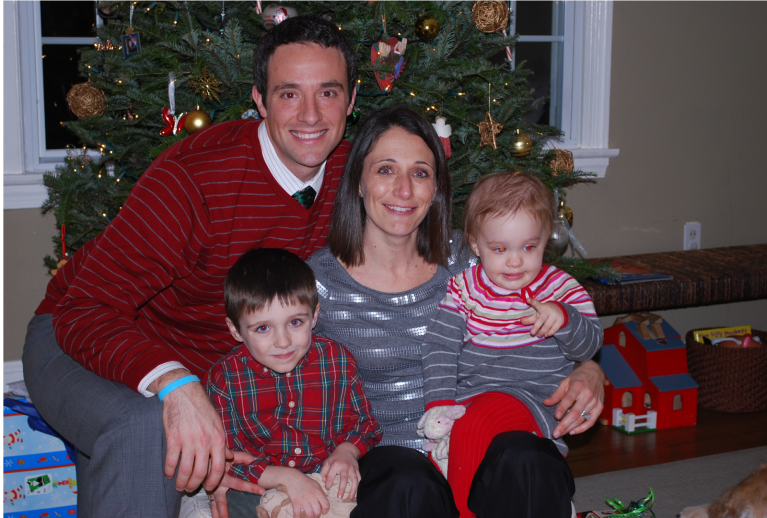 A family of four poses under a Christmas tree.