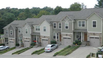 A block of connected townhouses in a neighborhood setting. Some have vehicles in their driveway. 