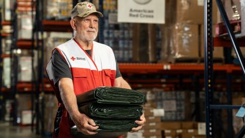 American Red Cross volunteer carrying green tarps in warehouse