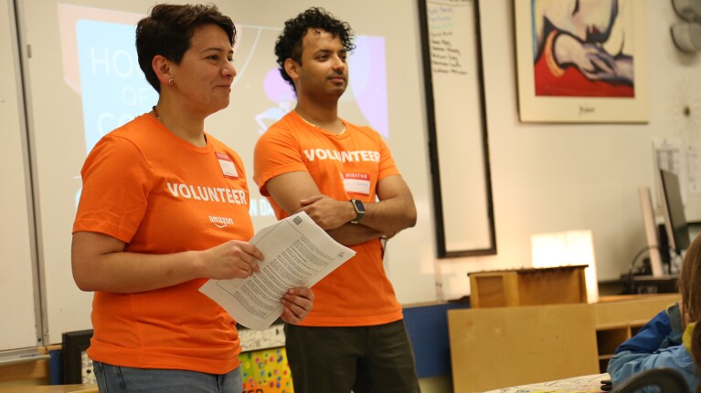 A photo of two Amazon volunteers speaking in front of a classroom.