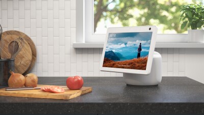 An image of an Echo Show device sitting on a kitchen counter top. A cutting board with food on it sits next to the device.