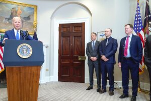 A photo of President Joe Biden speaking at a White House podium with several AI technical leads.