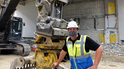 Oliver Reisenhofer mit Maske und Helm neben einem Bagger auf der Baustelle