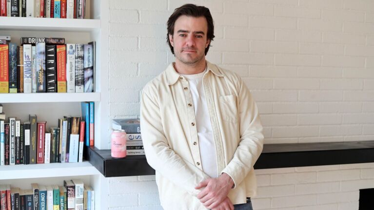 Man in beige jacket surrounded by bookshelves