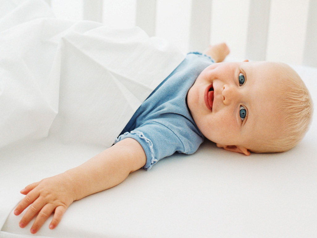 Baby smiling while lying on his back in his cot.