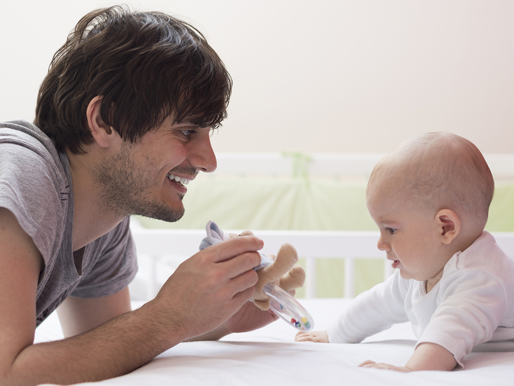 Smiling father showing confused baby a toy