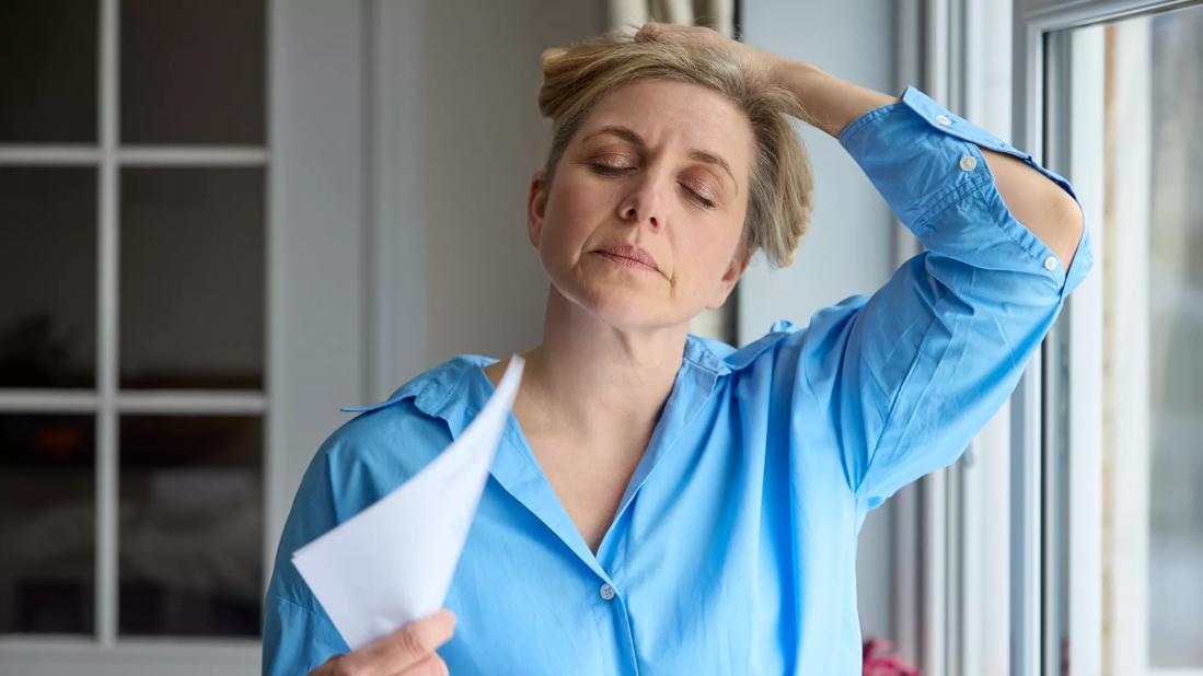 Female holding hair up at neck, eyes closed, fanning herself with piece of paper