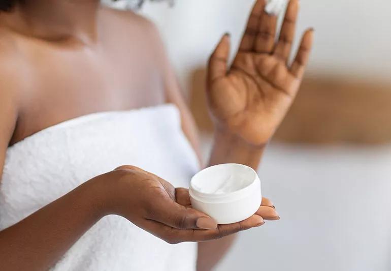 Person holding moisturizing cream container while applying it to their skin.