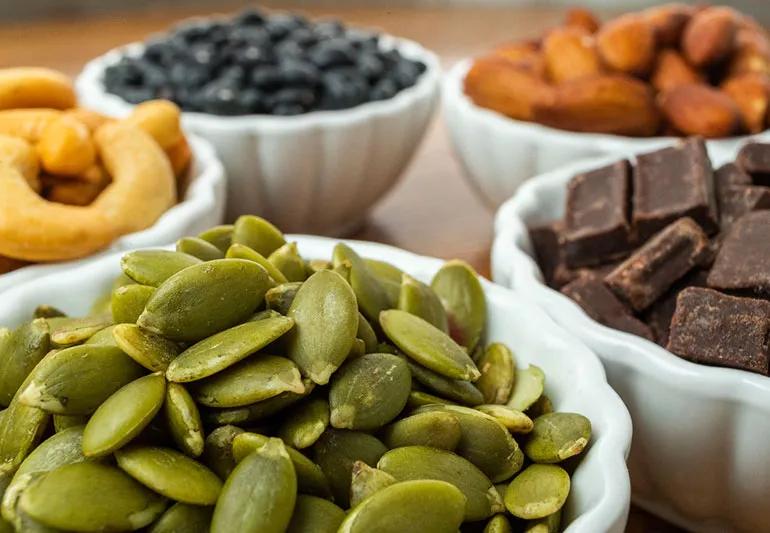 White bowls full of pumpkin seeds, dark chocolate and various kinds of nuts