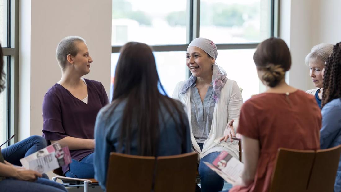 Group of women sitting in chairs in circle, some holding brochures, at cancer support group