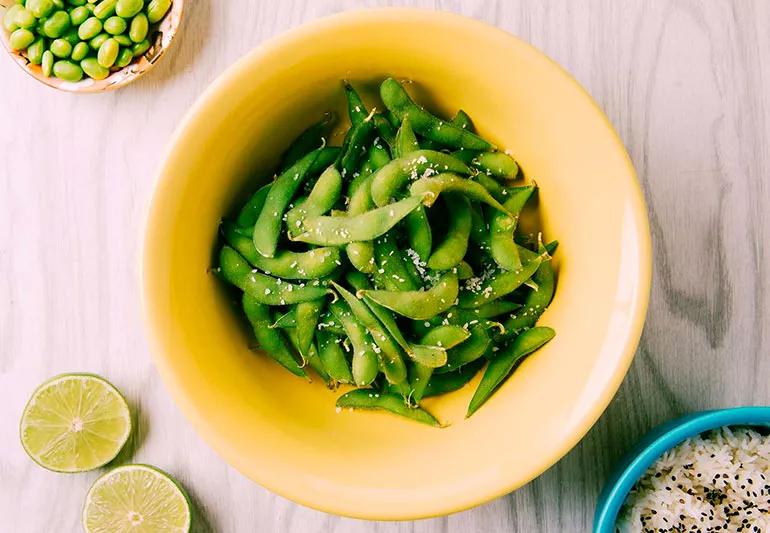 An overhead shot of a bowl of edamame sprinkled with salt