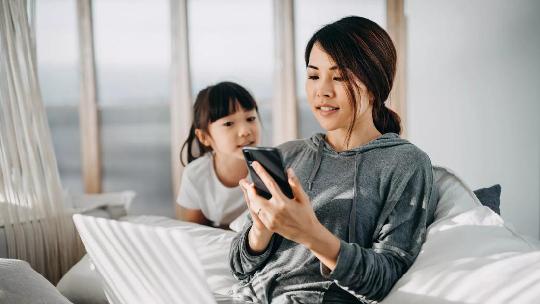 Child watching caregiver posting on phone and laptop