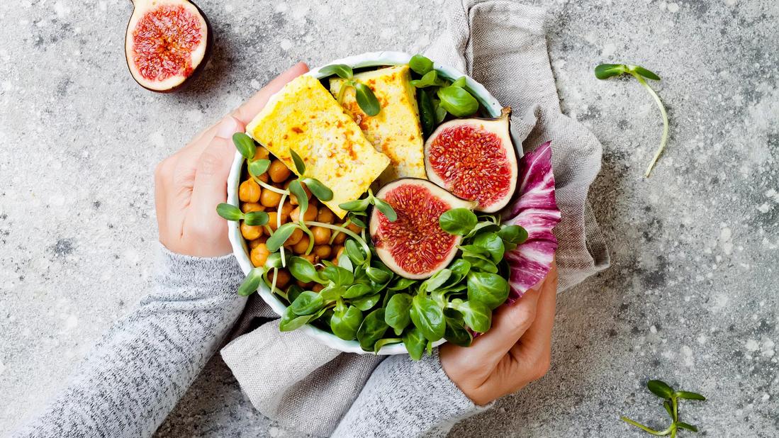 Hands cupping bowl of greens, chickpeas, whole figs, halved and tofu