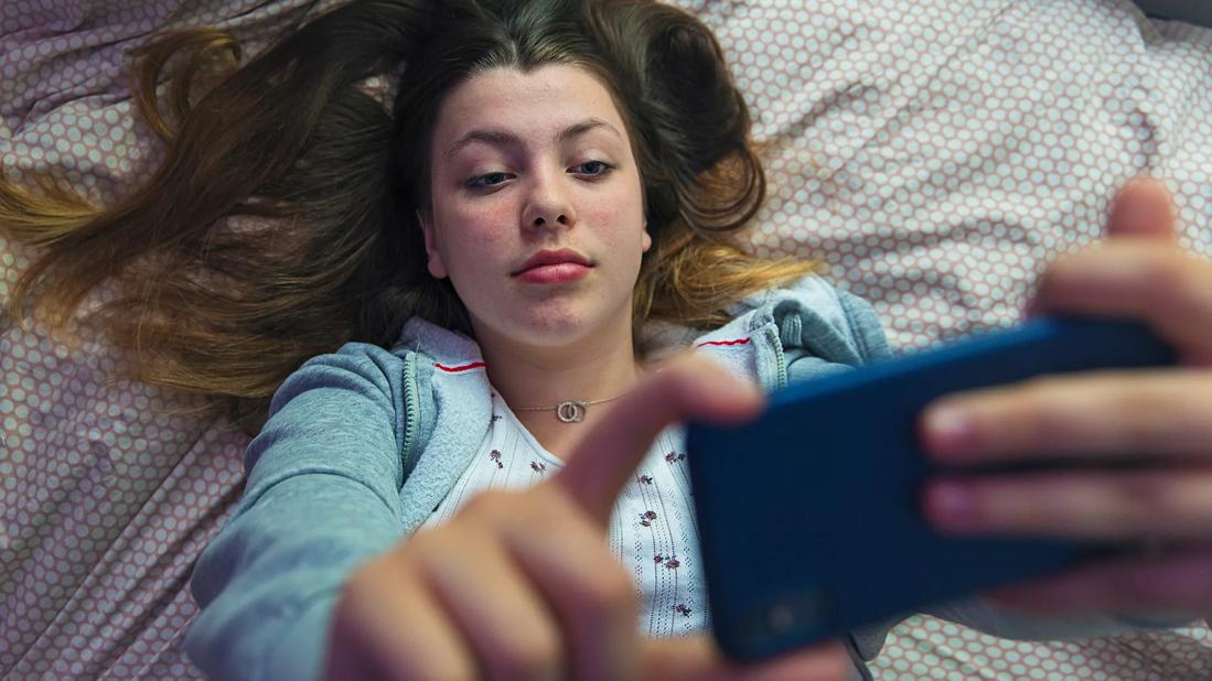 Teen lying on bed holding cell phone up reading it