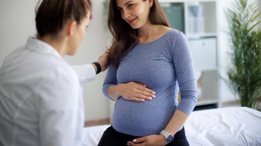 Smiling pregnant person speaking with healthcare provider in medical office