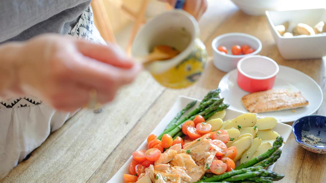 Person preparing healthy fish platter with veggies in kitchen