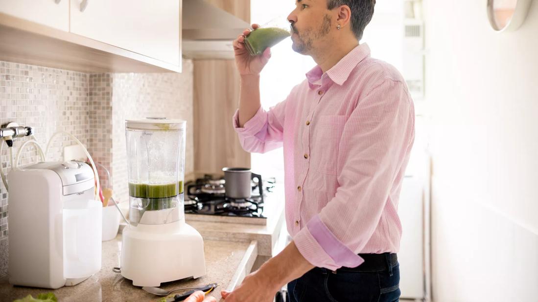 Person drinking smoothie in kitchen, with blender on counter