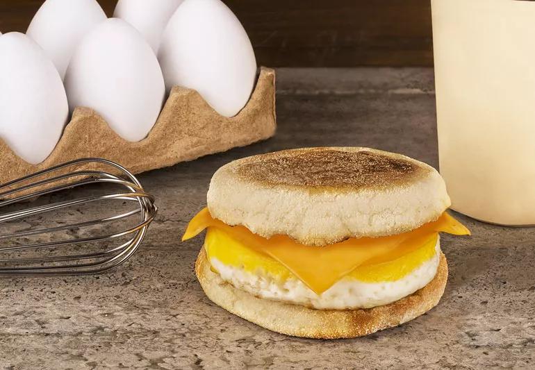 Egg and cheese English muffin sandwich on table, with eggs nearby