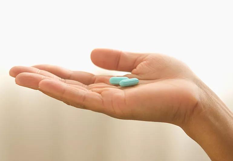 Hand holding two blue pills