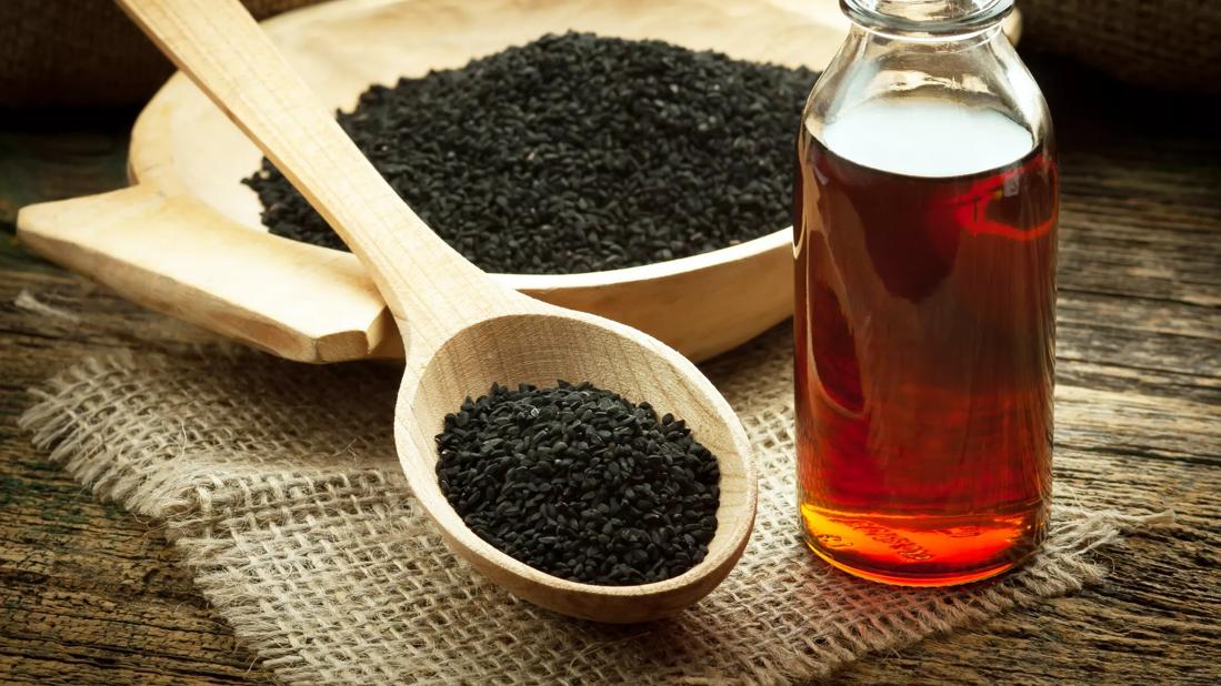 Black seed oil in bottle, with seeds in wooden spoon and bowl