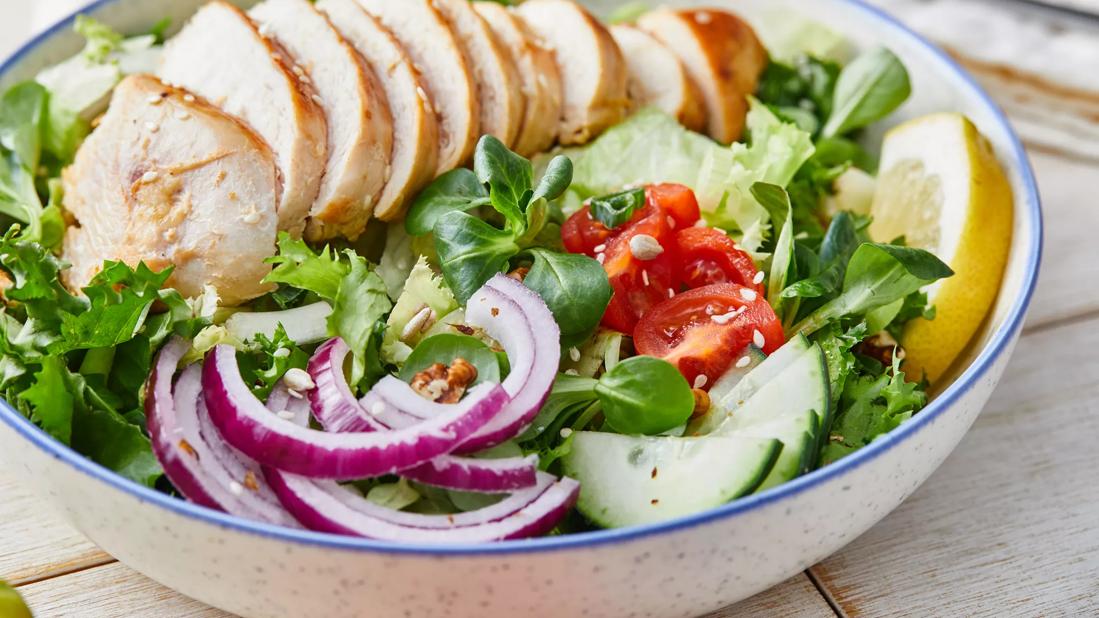 Sliced grilled chicken over salad