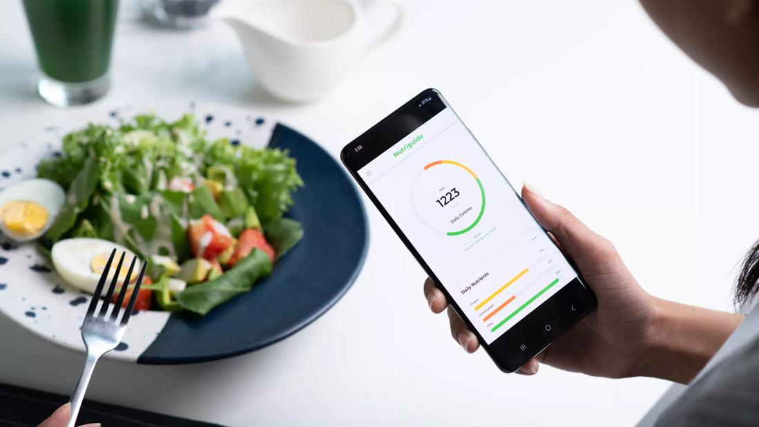 Person monitoring nutritional intake on smartphone app while eating a salad