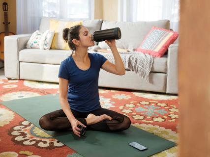 Person sitting on yoga mat in living room, drinking from bottle of water, cell phone on mat