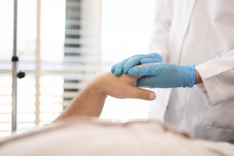 Healthcare provider in gloves holding hand of patient in hospital bed