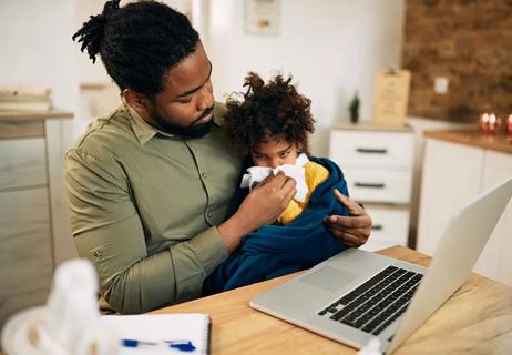 An adult sitting at a table while holding a child and helping them blow their nose