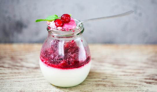 Red berry sauce over glass container of yogurt, with spoon balanced on top