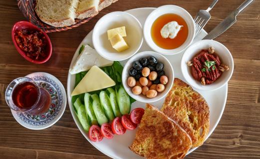 Plate full of an array of snack foods like vegetables, fruits, nuts, pickles, cheese and bread