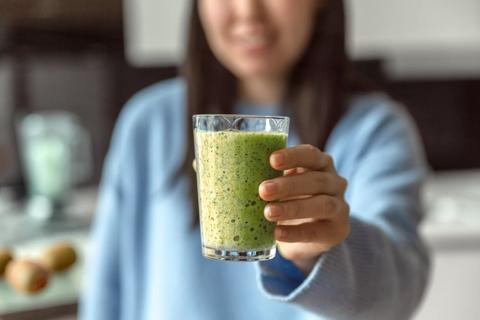 Person holding up glass of green-colored smoothie