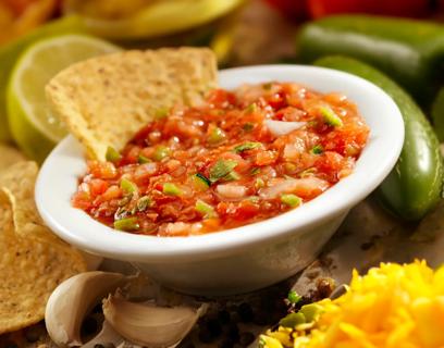 Small bowl of salsa, with chips, peppers, lime and garlic around bowl