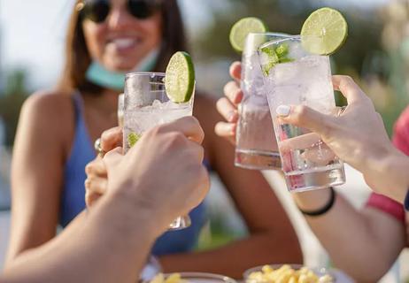 Friends cheers outside, tapping their cold drinks together.