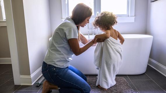 Caregiver drying off toddler with a towel in front of bathtub