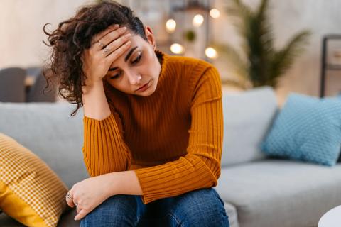 Person sitting on couch with head in hand, looking upset/stressed