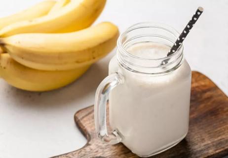 Milkshake in mason jar with straw, with bananas on the table