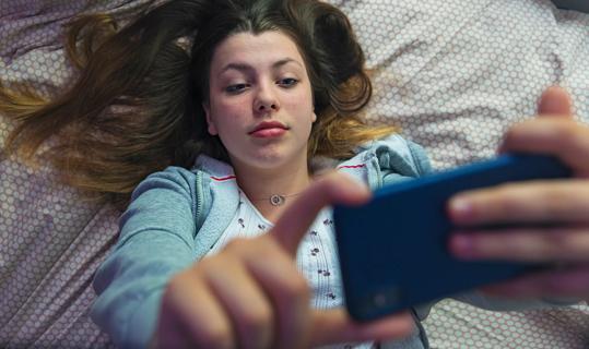 Teen lying on bed holding cell phone up reading it