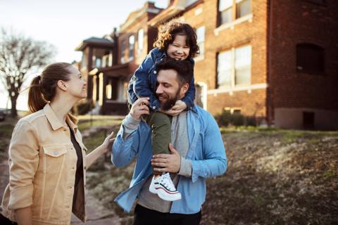 Two caregivers, with one holding a child on shoulders, walking happily outside